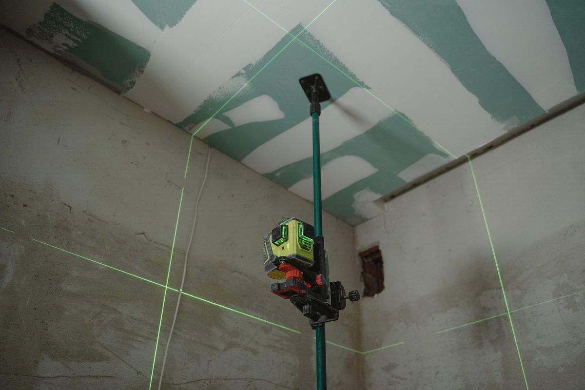 Een laserwaterpas tekent groene lijnen op muren en een plafond van gipsplaten