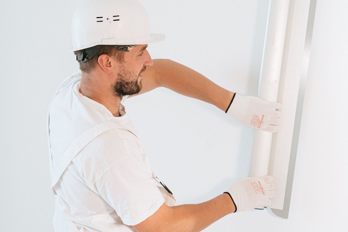 Vakman strijkt een witte muur glad met een lange pleisterspaan