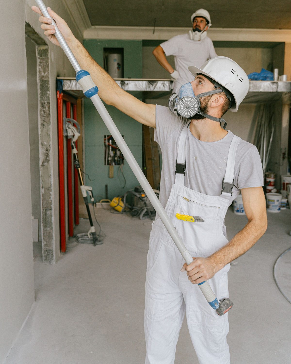 Twee vaklui in witte werkkleding werken een plafond en muren af